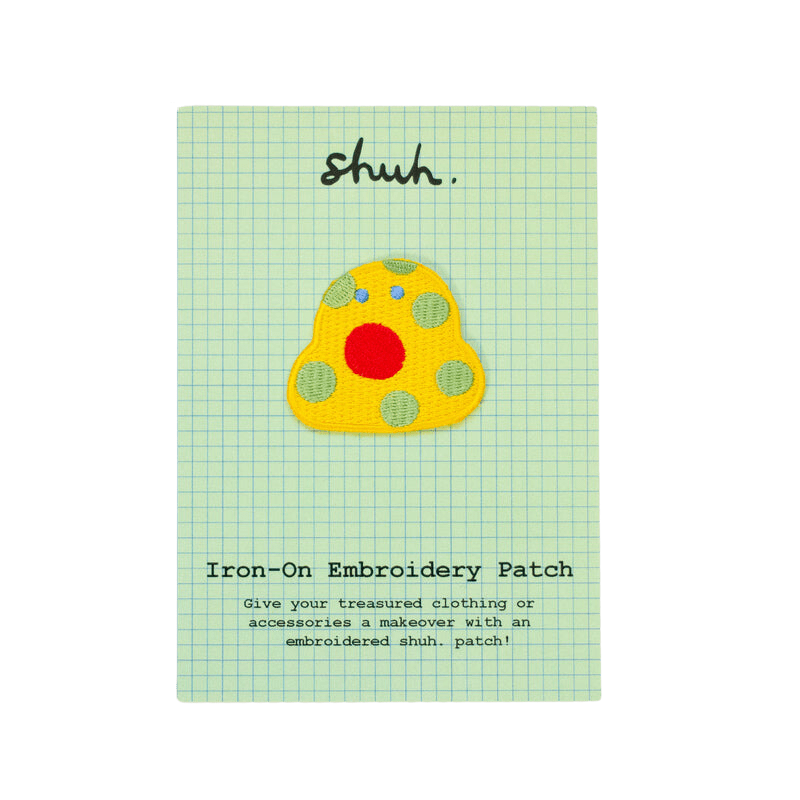 Shuh Embroidery Patch: A quirky little yellow blob with pastel green spots, tiny blue eyes and a large circular red mouth.