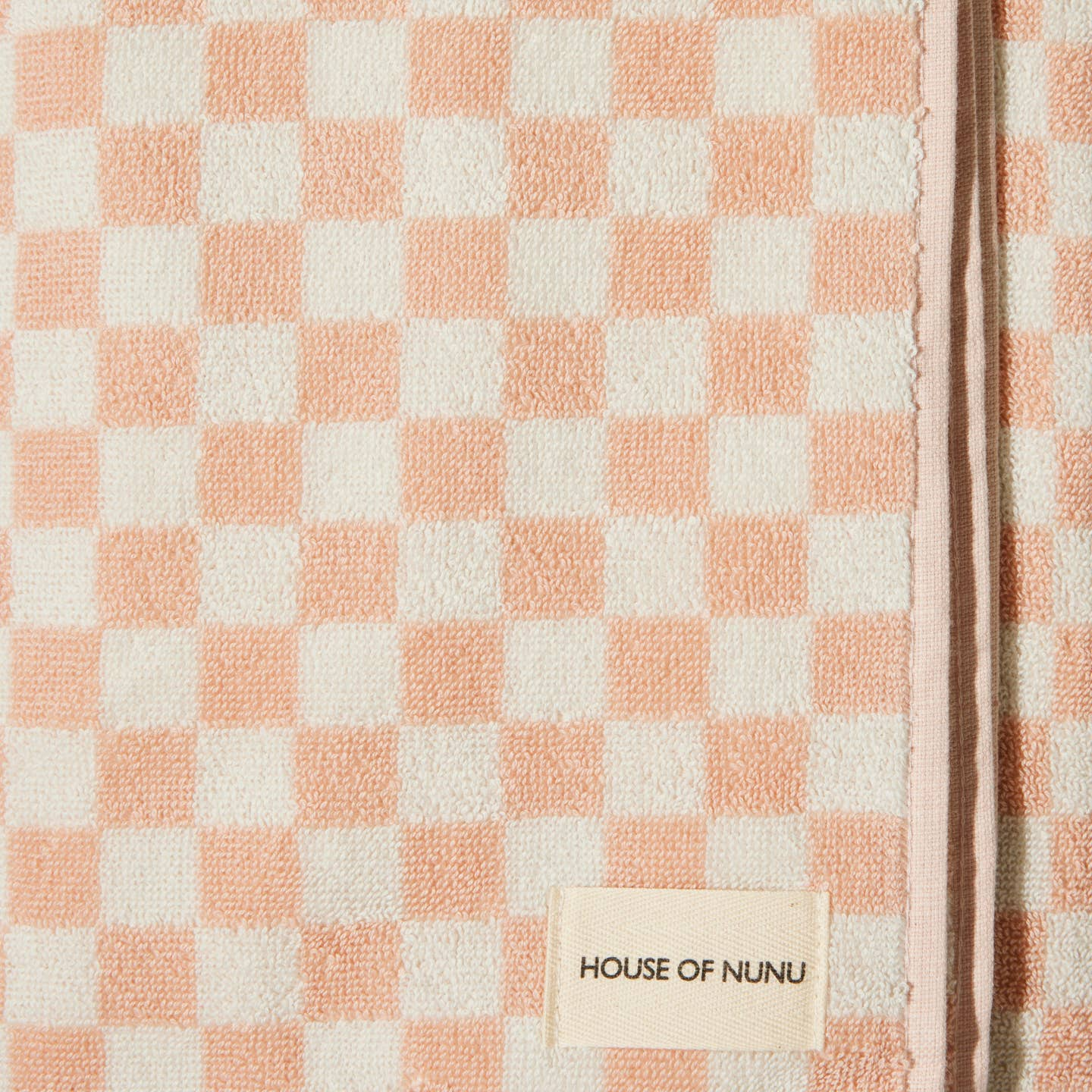 A close up of a bath towel in Pink Check by House of Nunu. This towel is white with soft peach checks and folded into a perfect rectangle.