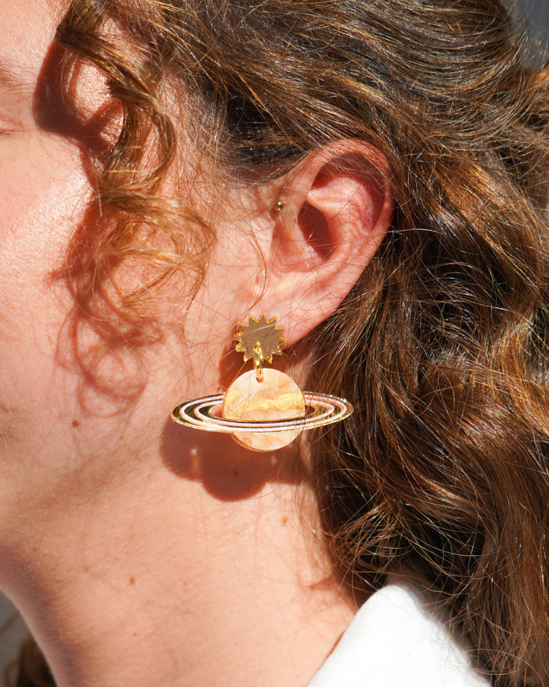 Flowatures Saturn Return dangle earrings being worn by a model with soft curls around her ear and face in the sunshine.