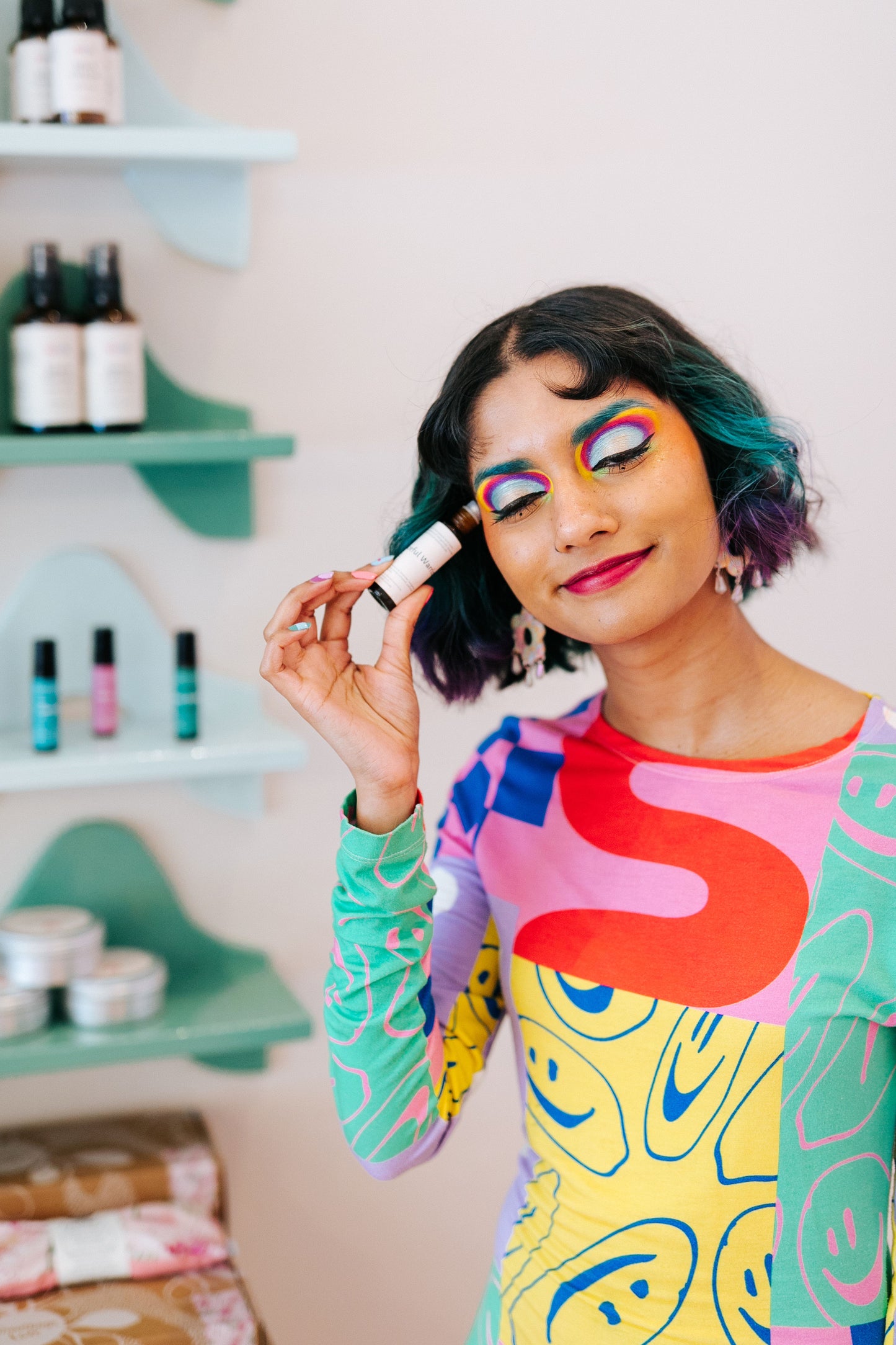 A Nimki Natural Perfume being applied to the temple by Nimki model Eishi. She has bright, neon eyeshadow and green & purple hair as she softly smiles applying the pulse point.