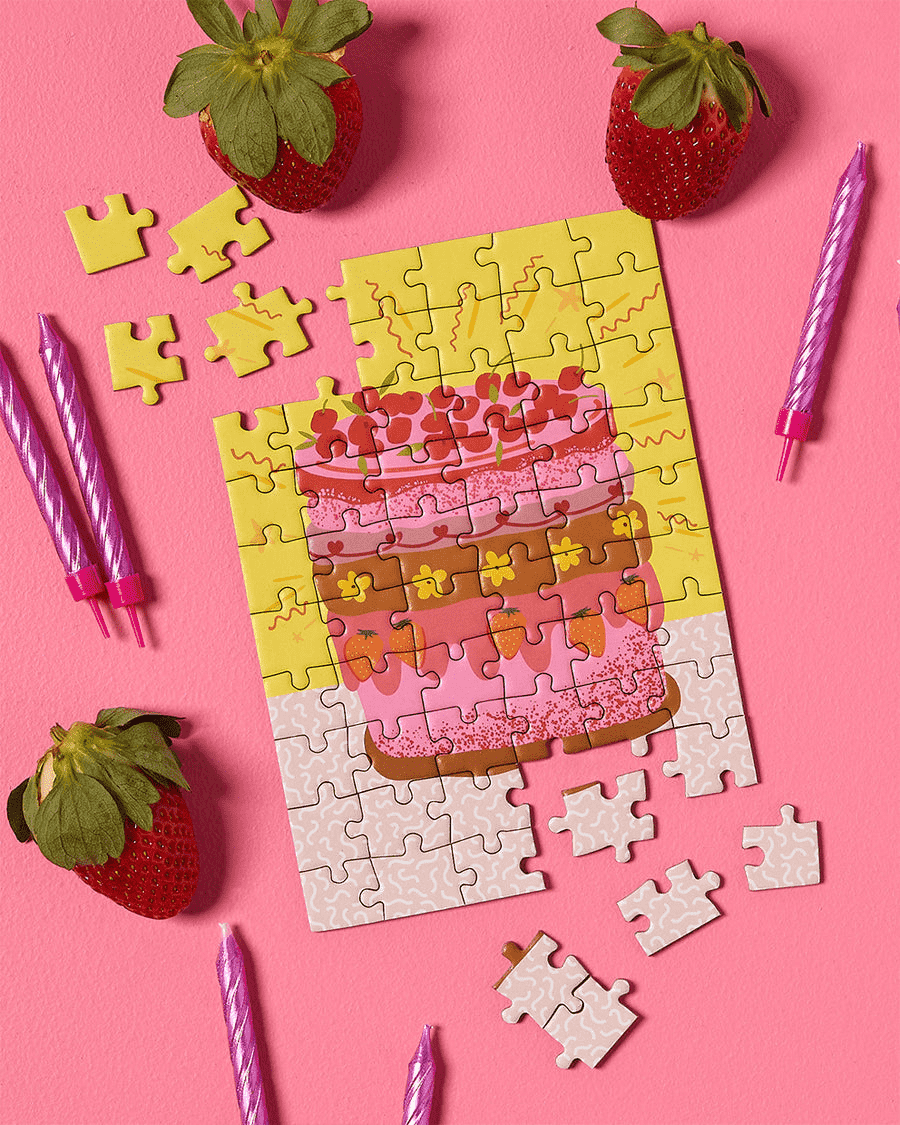 Greeting card puzzle: A super cute design of a multicoloured retro cake with flowers, strawberries and cherries on a yellow background with tiny squiggles around the outside.