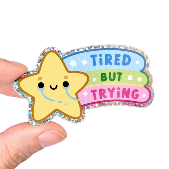 A tiny crying star sticker with a rainbow in it's wake reading: Tired But Trying
