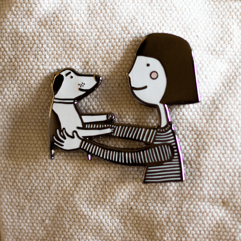 A cute pin of a girl (black hair, a soft smile and rosy red cheeks) holding her dog up in an embrace.