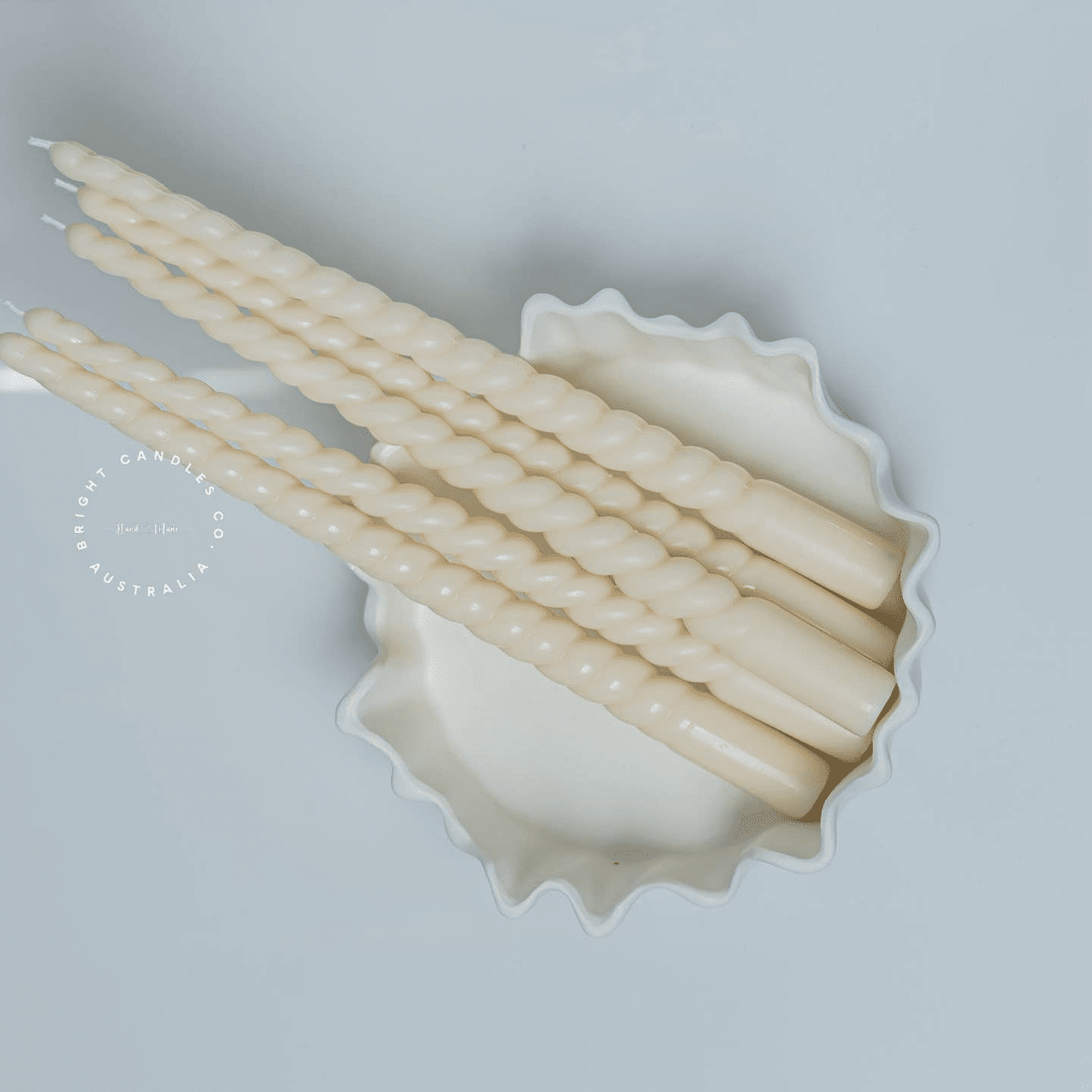 A stack of thin taper pillar candles in a white bowl. They have a soft curve running all the way through them.
