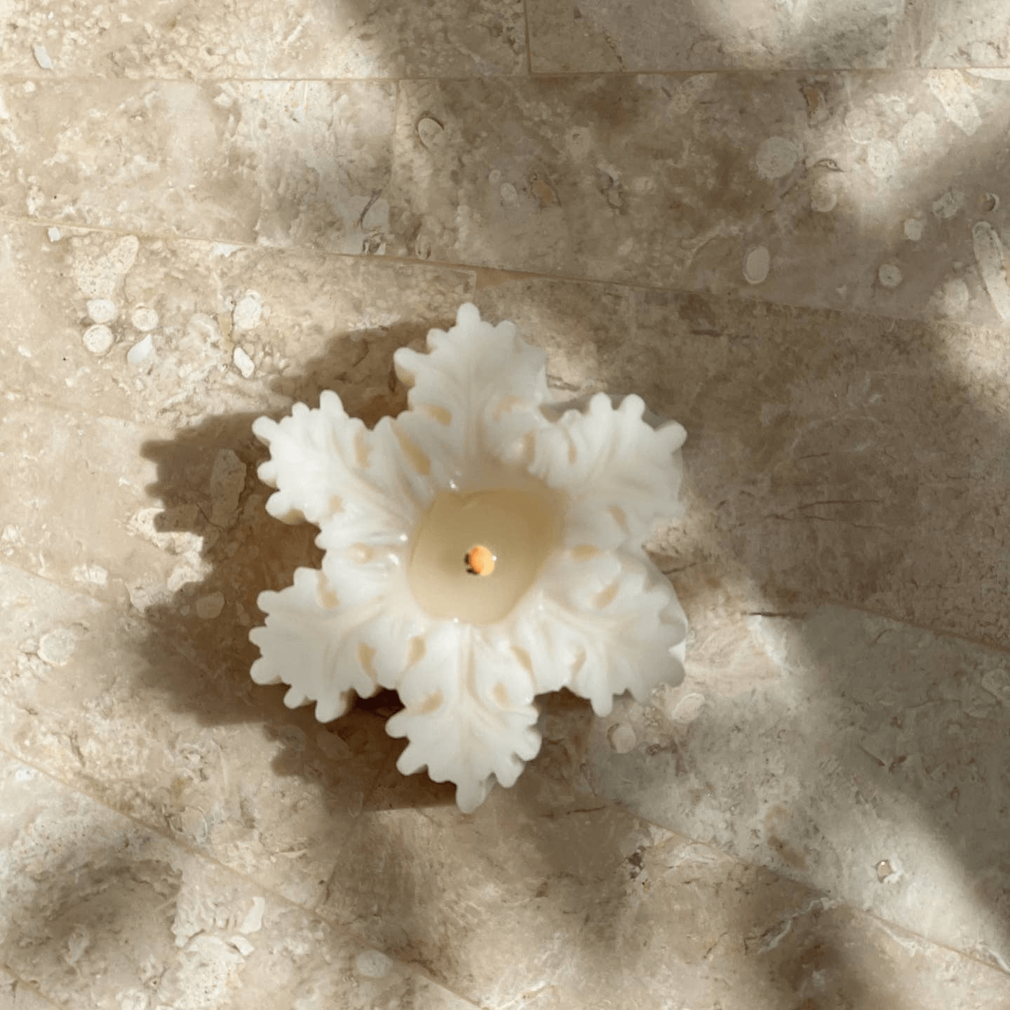 A beautiful handcrafted, pristine white snowflake candle burning on a terracotta plate.