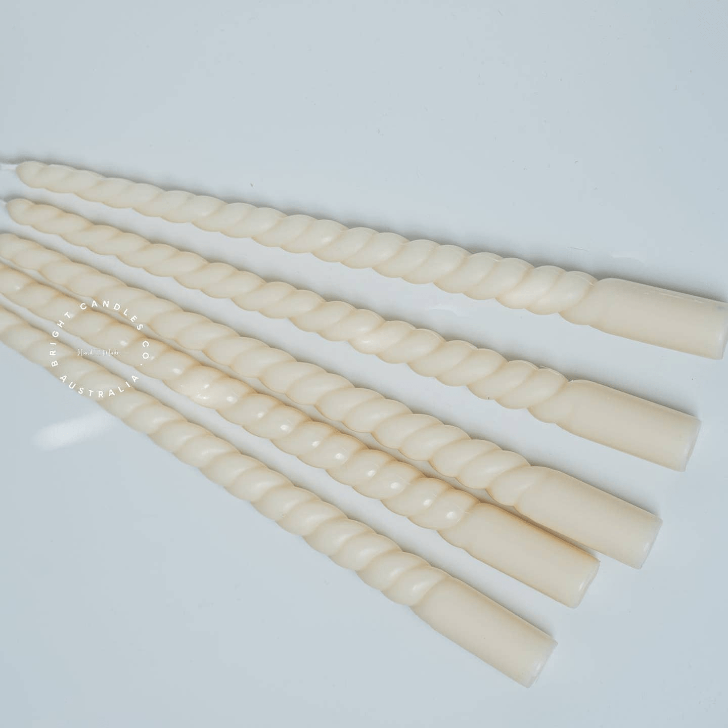 A stack of thin taper pillar candles in a white bowl. They have a soft curve running all the way through them.