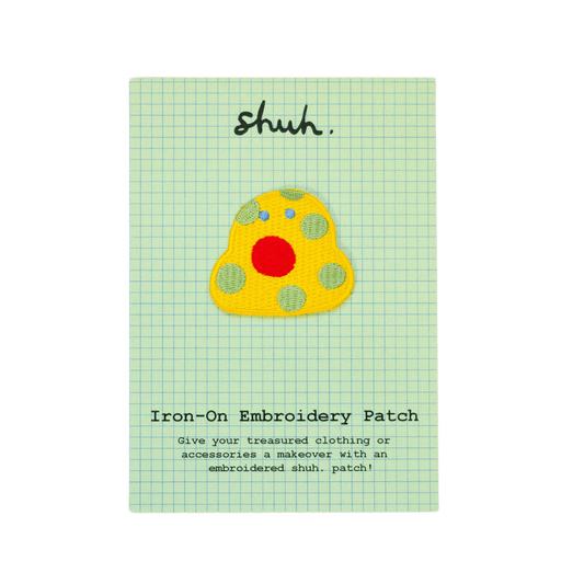 Shuh Embroidery Patch: A quirky little yellow blob with pastel green spots, tiny blue eyes and a large circular red mouth. 