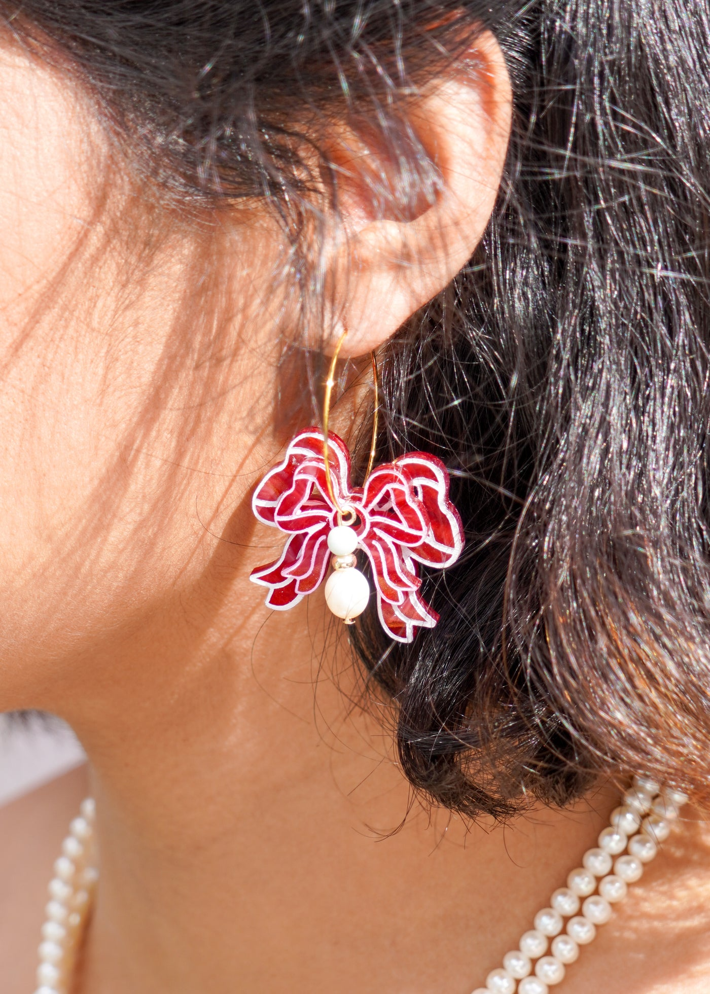 A gold hoop earring with a delicate red and white bow connected to two small pearls by Flowature. 