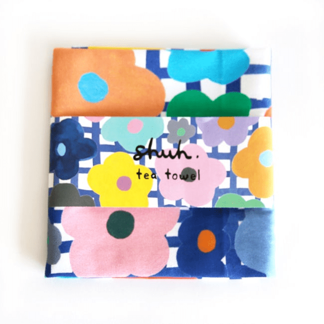 Shuh Lee's colourful Flower Tea Towel, adorned with bright multicoloured flowers folded. 