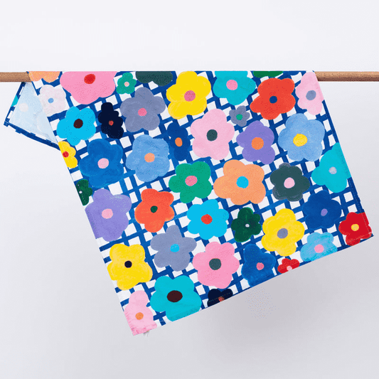 Shuh Lee's colourful Flower Tea Towel, adorned with bright multicoloured flowers and a blue grid background. 