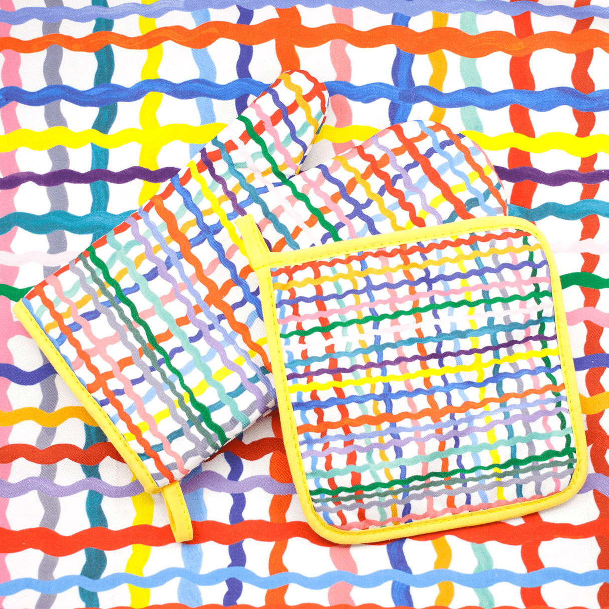 Shuh Lee Wave Pot Holder & matching oven Mitt photographed together. This super cute duo have a yellow trim with a patchwork pattern featuring colourful, wiggle lines. 