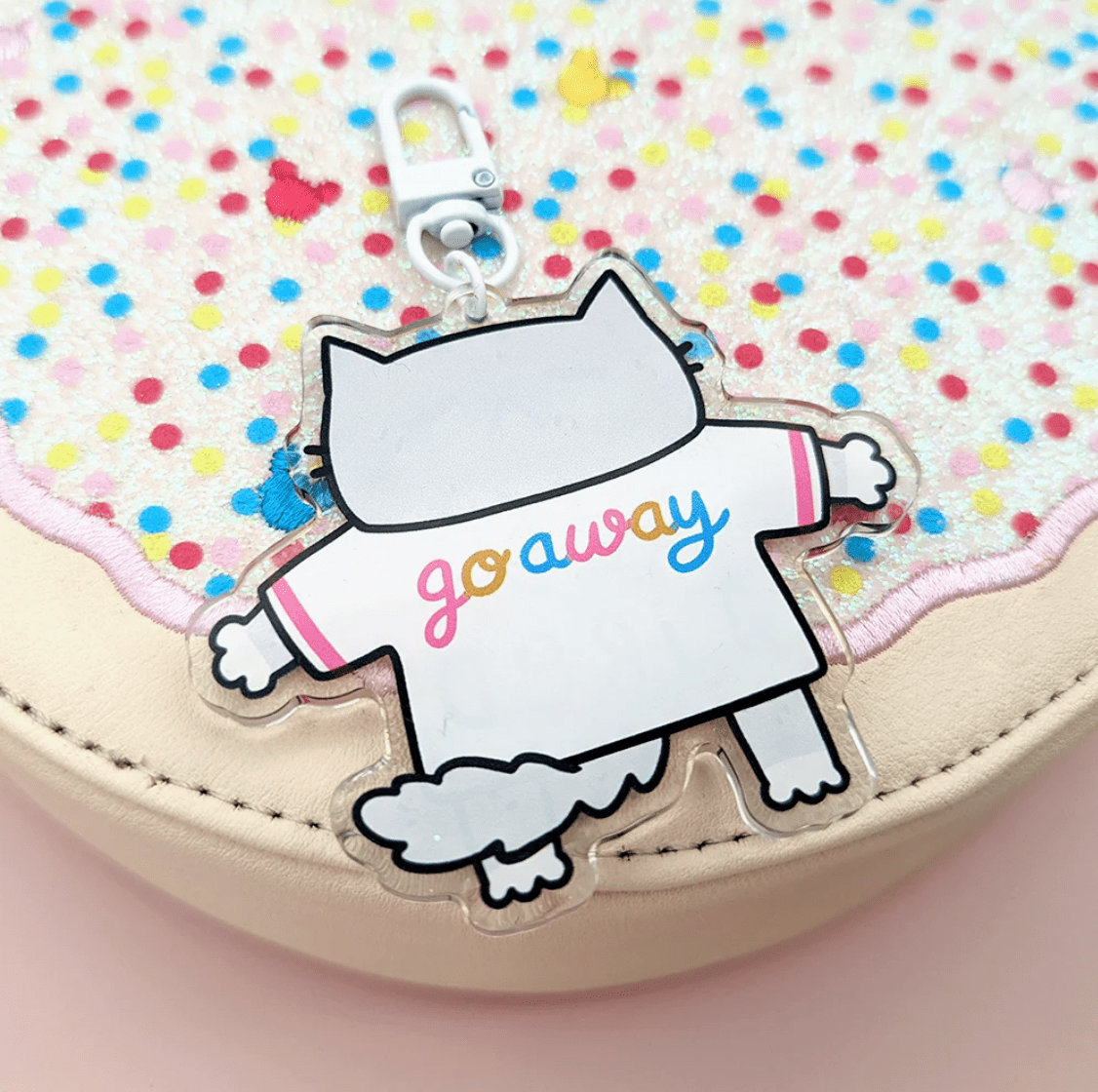 A super cute keychain by Fox & Cactus: a sleeping cat with pink cheeks and a heart note with a tee shirt that reads "Old & Tired" on the front and "Go Away" on the back. 