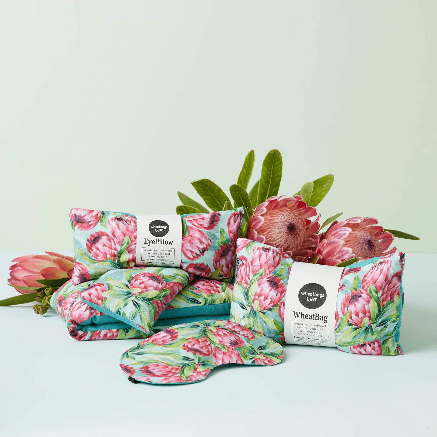 A collection of Wheatbag Love's eyepillows, masks and wheat bags all featuring the Protea print with beautiful fresh proteas in the foreground. 